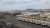 An artistic rendering of row of parts of wind turbines on a dock with the New York skyline in the background